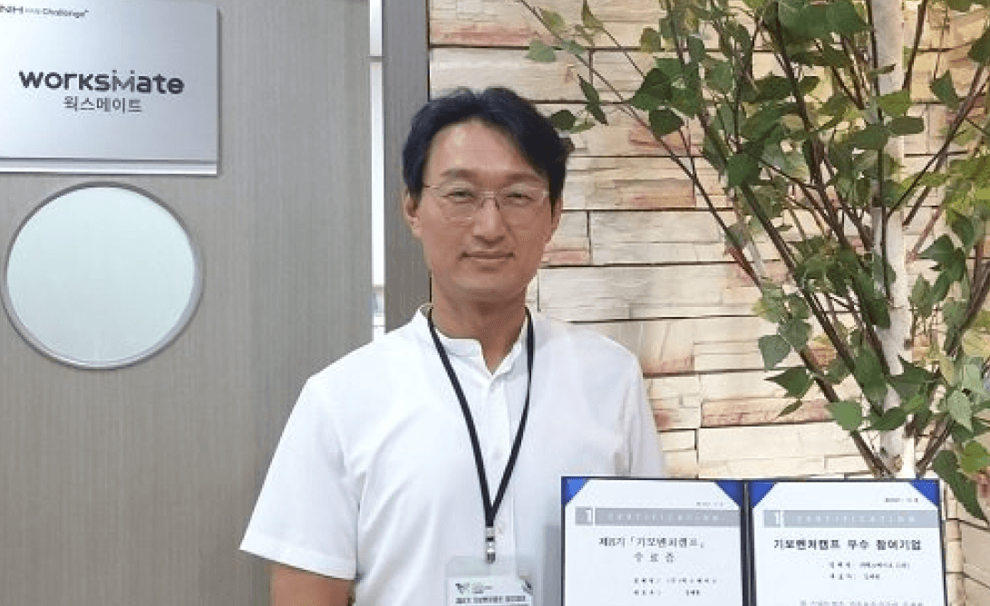 웍스메이트 사무실 앞에서 기보벤처캠프 수상 인증서를 들고 있는 남성 직원