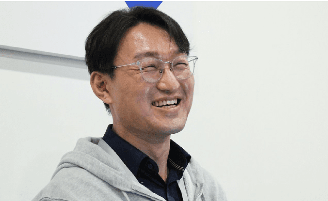 안경을 쓴 남성이 밝은 표정으로 웃고 있는 모습